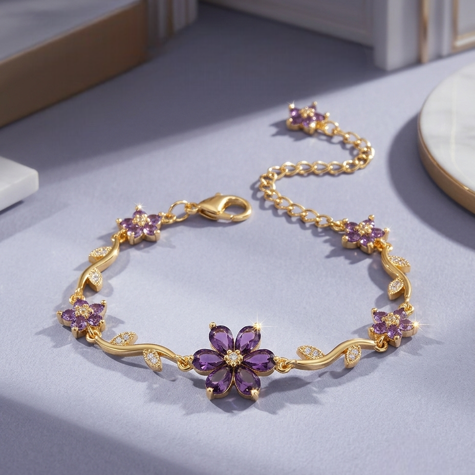 A gold chain bracelet with purple flower-shaped crystals and small clear accent stones, displayed on a light lavender surface.