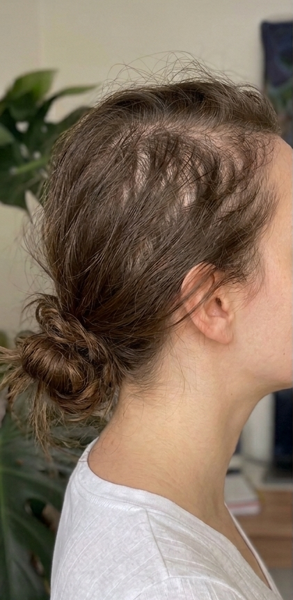 Person with a bun hairstyle indoors, wearing a light-colored top.