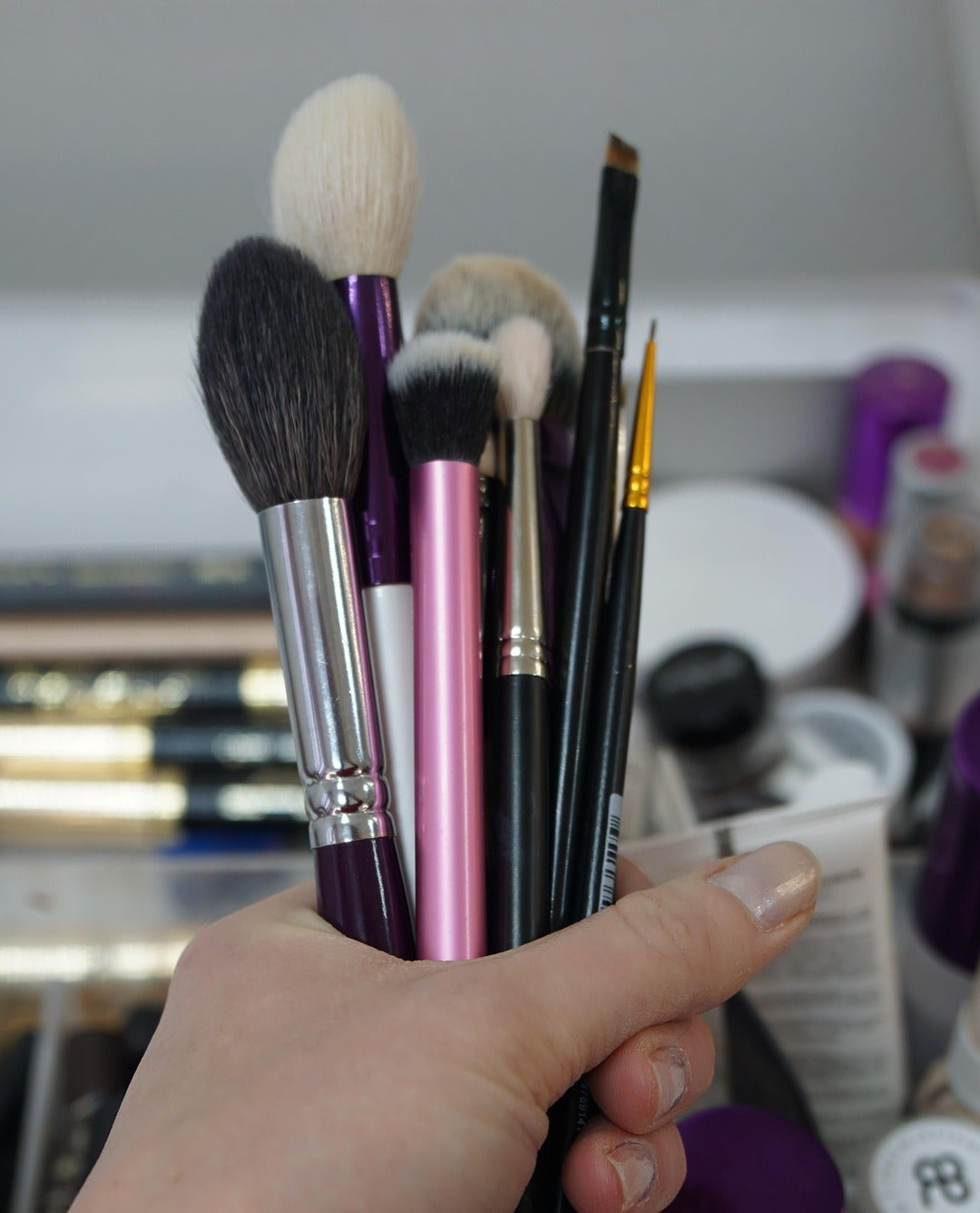 Hand holding a collection of makeup brushes with a blurred background